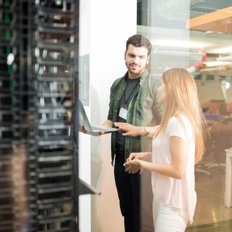 Two business people standing in server room with laptop and discussing